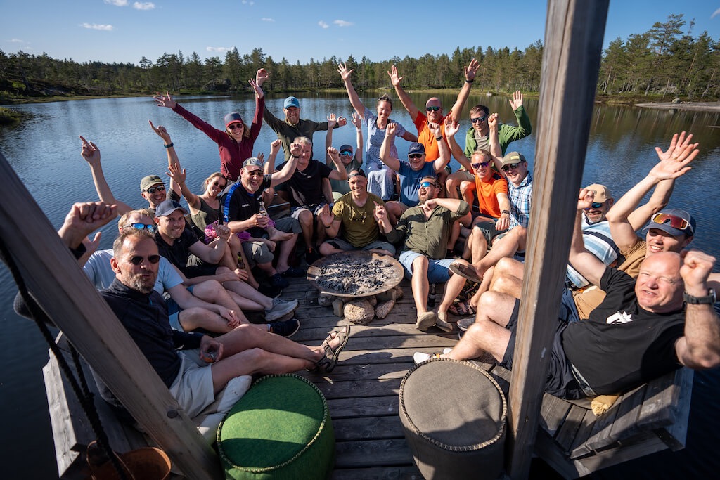 Kodemakere vinker til kamera fra en flåte på et vann en sommerdag.
