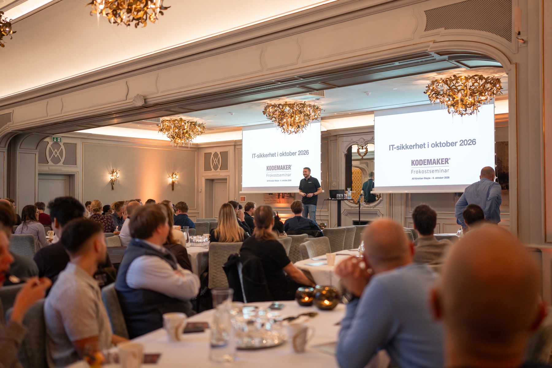 Frokostseminar på Hotel Continental, publikum ved runde bord og foredragsholder foran to lerreter.